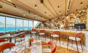 Restaurant med udsigt over havet, borde og stole, samt en veludstyret bar. (AI-genereret tekst)