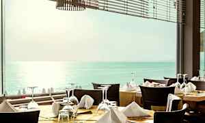 Restaurant med dækkede borde foran et vindue med udsigt over havet. (AI-genereret tekst)
