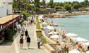 En gangsti ved havet med mennesker, der går, og personer, der slapper af på liggestole under parasoller. (AI-genereret tekst)