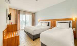 Moderne hotelværelse med to senge, lyse farver og store vinduer. (AI-genereret tekst)