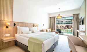 Hotelværelse med dobbeltseng, sofa og udsigt til en pool. (AI-genereret tekst)