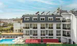 Et hotel med hvid facade og flere vinduer og altaner, en pool foran bygningen. (AI-genereret tekst)