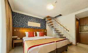 Et hotelværelse med to senge, dekorativt tapet og en vindeltrappe, der fører opad. (AI-genereret tekst)