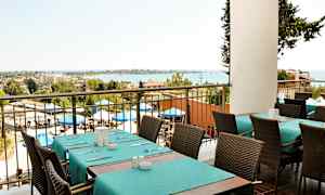 Udsigt fra en restaurant med dækkede borde og stole, udendørsområde med parasoller og havet i baggrunden. (AI-genereret tekst)