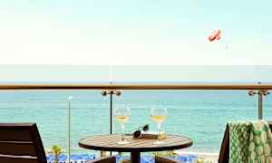 En altan med bord, to glas og en bog med udsigt over havet. (AI-genereret tekst)