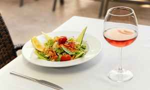 En tallerken med salat og et glas rosévin på et dækket bord. (AI-genereret tekst)