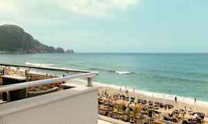 Et billede af en strand med liggestole, parasoller og mennesker, der svømmer i havet. I baggrunden ses en klippe. (AI-genereret tekst)