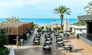 En udendørsrestaurant med borde og stole, beliggende tæt på havet. (AI-genereret tekst)