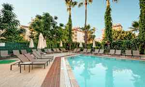 Udendørs swimmingpool ved et hotel omgivet af liggestole og parasoller. (AI-genereret tekst)