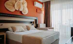 Hotelværelse med orange væg, dobbeltseng med to puder og dekorative genstande over sengen. (AI-genereret tekst)