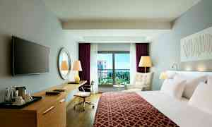 Et moderne hotelværelse med en seng, skrivebord, lænestol og balkon med udsigt. (AI-genereret tekst)