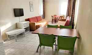 Et opholdsområde med sofaer, et spisebord med stole og et vægmonteret tv. (AI-genereret tekst)