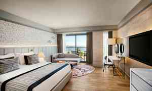 Et hotelværelse med en stor seng, siddeområde og en balkon ud mod havet. (AI-genereret tekst)