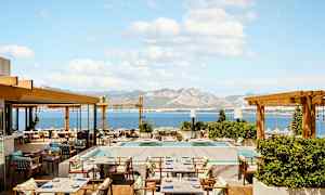 En restaurantterrasse med havudsigt og bjerge i baggrunden. (AI-genereret tekst)