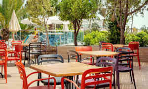 Farverige stole og borde arrangeret på en udendørs terrasse nær grønt og en pool. (AI-genereret tekst)