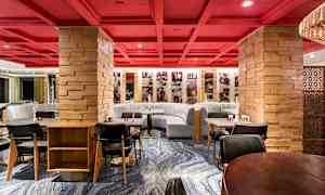 En restaurant med røde lofter og træstolper samt grå sofaer og moderne spiseborde. (AI-genereret tekst)