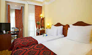 Hotelværelse med to enkeltsenge, røde dekorationer og gardiner. (AI-genereret tekst)