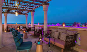 En overdækket terrasse med siddepladser og belysning, med udsigt over havet om aftenen. (AI-genereret tekst)