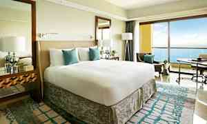 Et moderne hotelværelse med en stor seng, hvidt og turkis sengetøj, og en altan med udsigt over havet. (AI-genereret tekst)