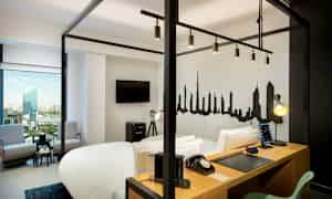 Et moderne hotelværelse med en himmelseng, skrivebord, TV, siddeområde og en bysilhuet malet på væggen. (AI-genereret tekst)