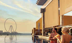 Personer står i en pool med udsigt til et stort pariserhjul ved solnedgang. (AI-genereret tekst)