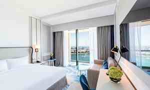 Hotelværelse med dobbeltseng og havudsigt gennem store vinduer. (AI-genereret tekst)