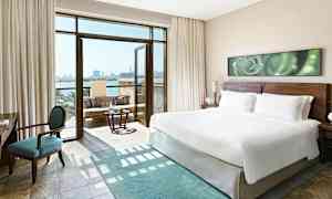 Moderne hotelværelse med en stor king size seng, en siddegruppe og åben balkon med havudsigt. (AI-genereret tekst)