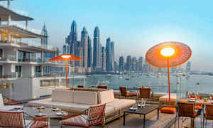 Et moderne udendørsområde med komfortable siddepladser og udsigt over en bysilhuet ved vandet. (AI-genereret tekst)