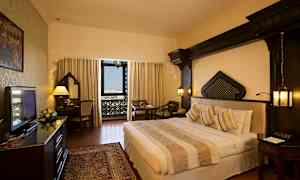 Et hotelværelse med en dobbeltseng, skrivebord og siddeområde. Vinduet har udsigt med dekorative detaljer. (AI-genereret tekst)