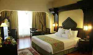 Et hotelværelse med en stor seng, mørke træs møbler og vinduer dækket af elegante gardiner. (AI-genereret tekst)