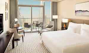 Et moderne hotelværelse med en stor seng, siddeområde og en balkon med udsigt over en stor by. (AI-genereret tekst)