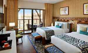 To redte senge i et hotelværelse med moderne indretning, store vinduer med balkon og udsigt. (AI-genereret tekst)