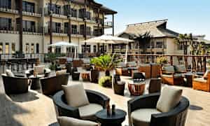 En udendørsterrasse med moderne siddepladser, parasoller og planter, omgivet af bygninger. (AI-genereret tekst)