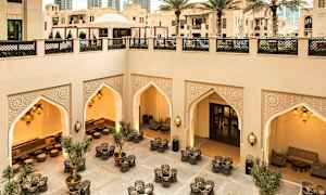 Veludformet gårdhave med siddegrupper, orientalske bueudsmykninger og belysning, omgivet af moderne og traditionel arkitektur. (AI-genereret tekst)