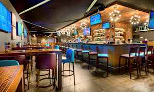 Interiør af en moderne bar med høje borde og stole samt flere tv-skærme på væggene. (AI-genereret tekst)