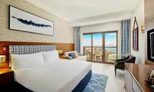 Et hotelværelse med en dobbeltseng, sofa og altan med udsigt over havet. (AI-genereret tekst)