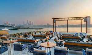 Udendørs loungeområde med udsigt over vandet og byens skyline. (AI-genereret tekst)