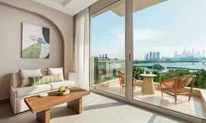 Interiør af stue med sofa og bord, samt udsigt over altan og bysilhuet. (AI-genereret tekst)