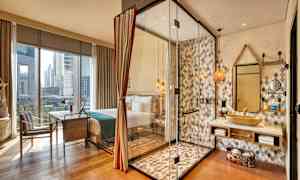 Et hotelværelse med store vinduer. Et bruseområde med glasvægge ses ved siden af en håndvask og spejl. (AI-genereret tekst)