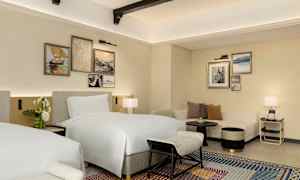 Et hotelværelse med to senge, sofa og dekorative billeder på væggen. (AI-genereret tekst)