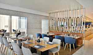 Billede af en moderne restaurant med flere opdækkede borde og stole i forskellige farver. Varm og stilfuld indretning. (AI-genereret tekst)