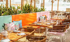 En udendørs spiseområde med dækkede borde, farverige puder og græsser. (AI-genereret tekst)