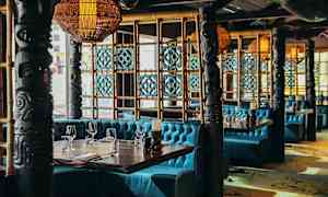En restaurantindretning med turkisfarvede sofaer, dekorative søjler og træpaneler. (AI-genereret tekst)