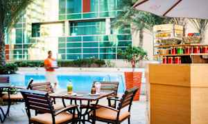 Et cafébord med to drikkevarer og en kage tæt ved en pool, omgivet af træer og glasvæg. (AI-genereret tekst)