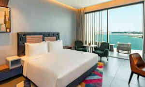 Et moderne hotelværelse med en stor seng, siddepladser og et stort vindue med udsigt over havet. (AI-genereret tekst)