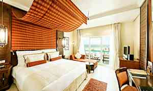 Et moderne og lyst hotelværelse med en stor seng, siddeområde og en møbleret balkon med udsigt over havet. (AI-genereret tekst)