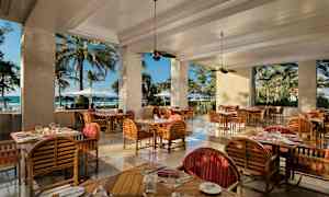 Restaurant med træmøbler og udsigt til stranden gennem store åbninger. (AI-genereret tekst)