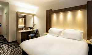 Et hotelværelse med en stor seng, en arbejdsplads med stol og et spejl. (AI-genereret tekst)