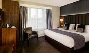 Et hotelværelse med stor seng, lænestol og træindretning. (AI-genereret tekst)