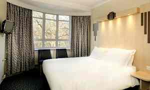 Et hotelværelse med en stor seng, to stole og et vindue med udsigt til træer. (AI-genereret tekst)